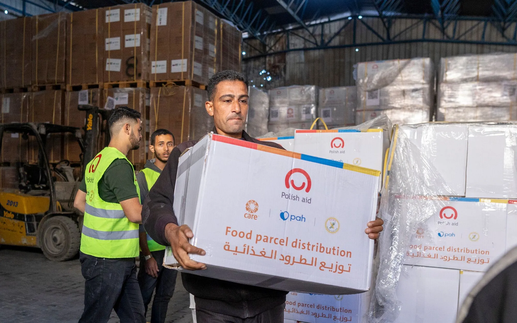 A man with a serious expression carries a large white box labeled 