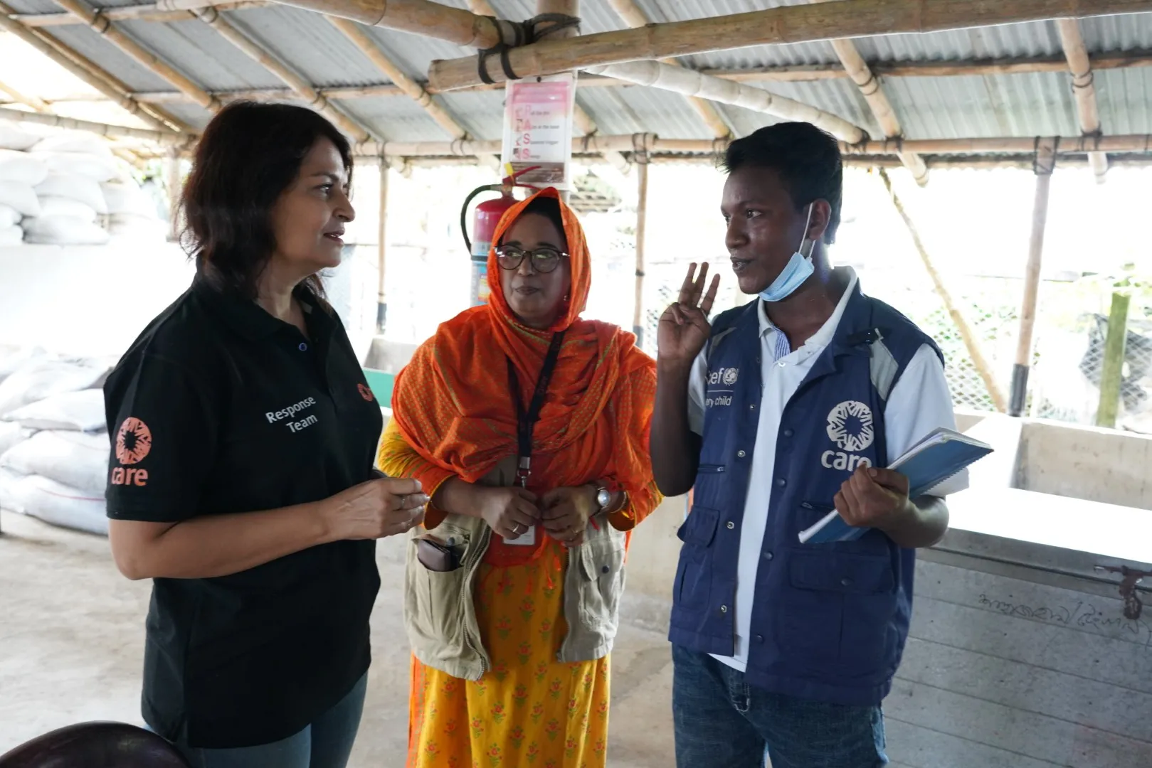 A woman and a man wearing emergency vests with the CARE logo are talking to each other, while another colleague in the middle listens attentively.