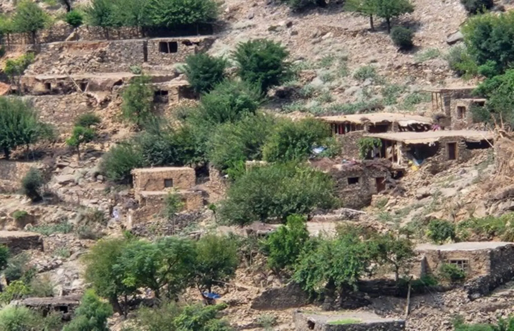 Aerial view of damaged mud-brick homes scattered across hillside terrain in Afghan village after earthquake.