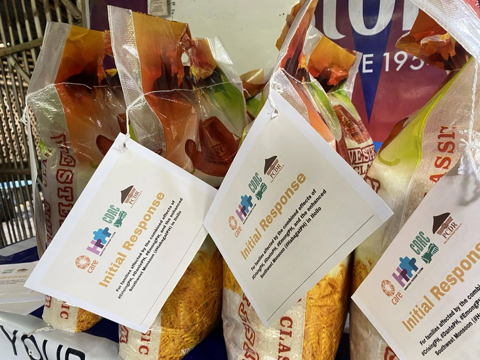 Bags of rice are tagged with Initial Response cards featuring logos from CARE and other partner organizations.
