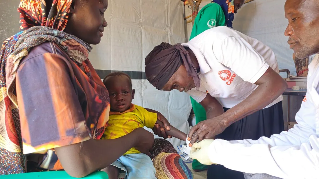 Two medical professionals work to treat a young child, held by his mother, in South Sudan.