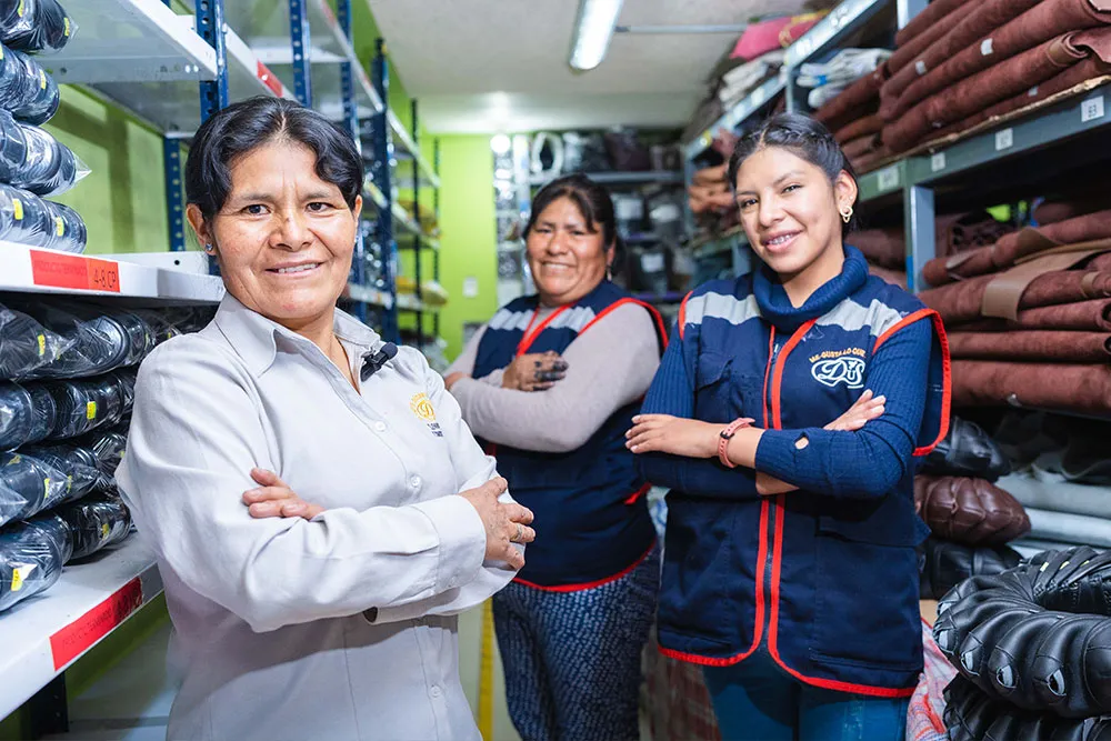 Three women, two of whom are wearing vests, stand together with their arms crossed in a store aisle.