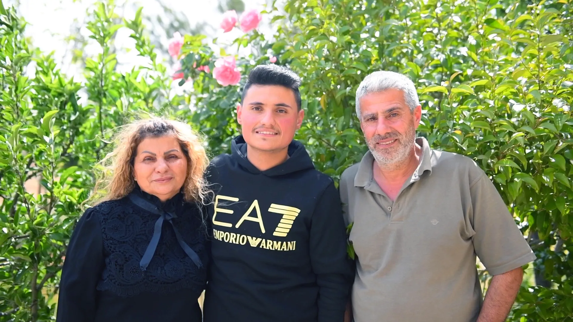 Portrait of woman, young man, and older man in front of flowers and greenery.