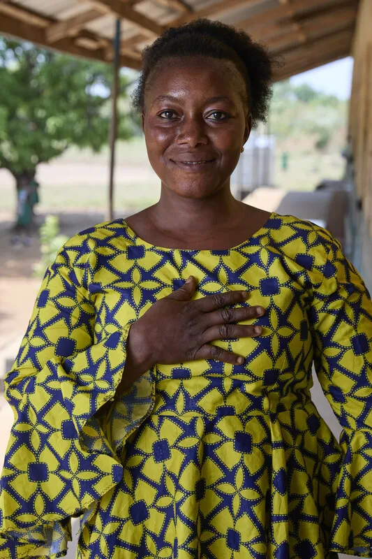 A woman in yellow smiles at the camera with her hand over her heart.