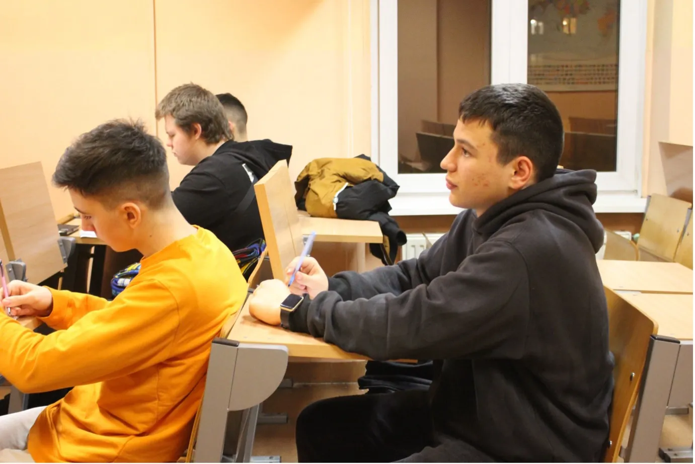 Four boys facing left, seated at desks in a classroom.