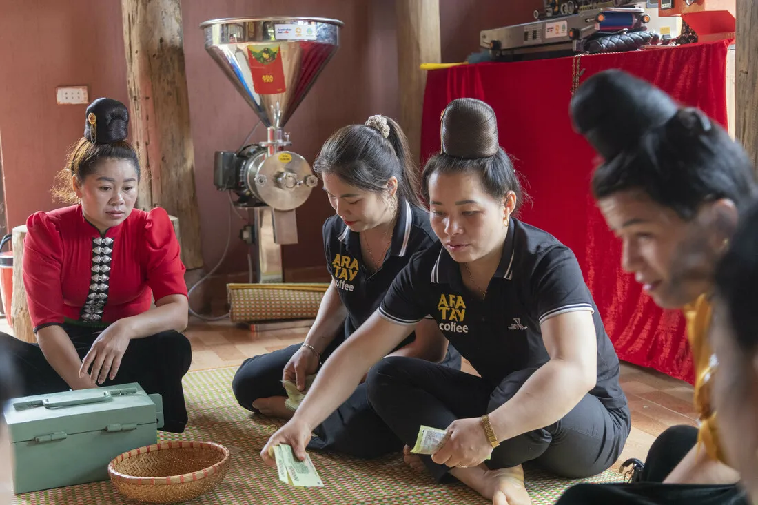 A group of women sitting on the ground facing the ground and a bowl holding items.