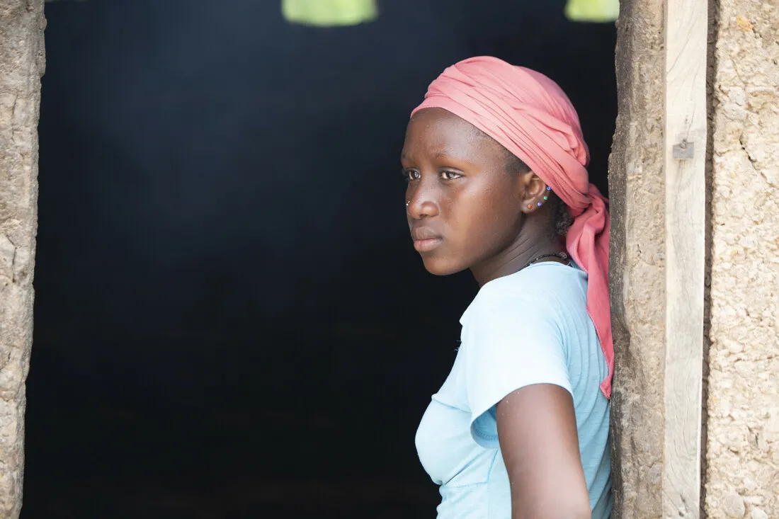 A young girl rests against a doorframe and looks into the distance.