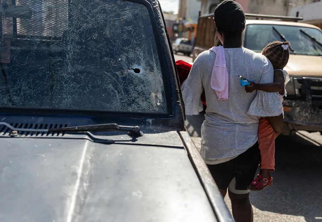Image of car with bullet hole in windshield, with woman, back to camera, holding child.
