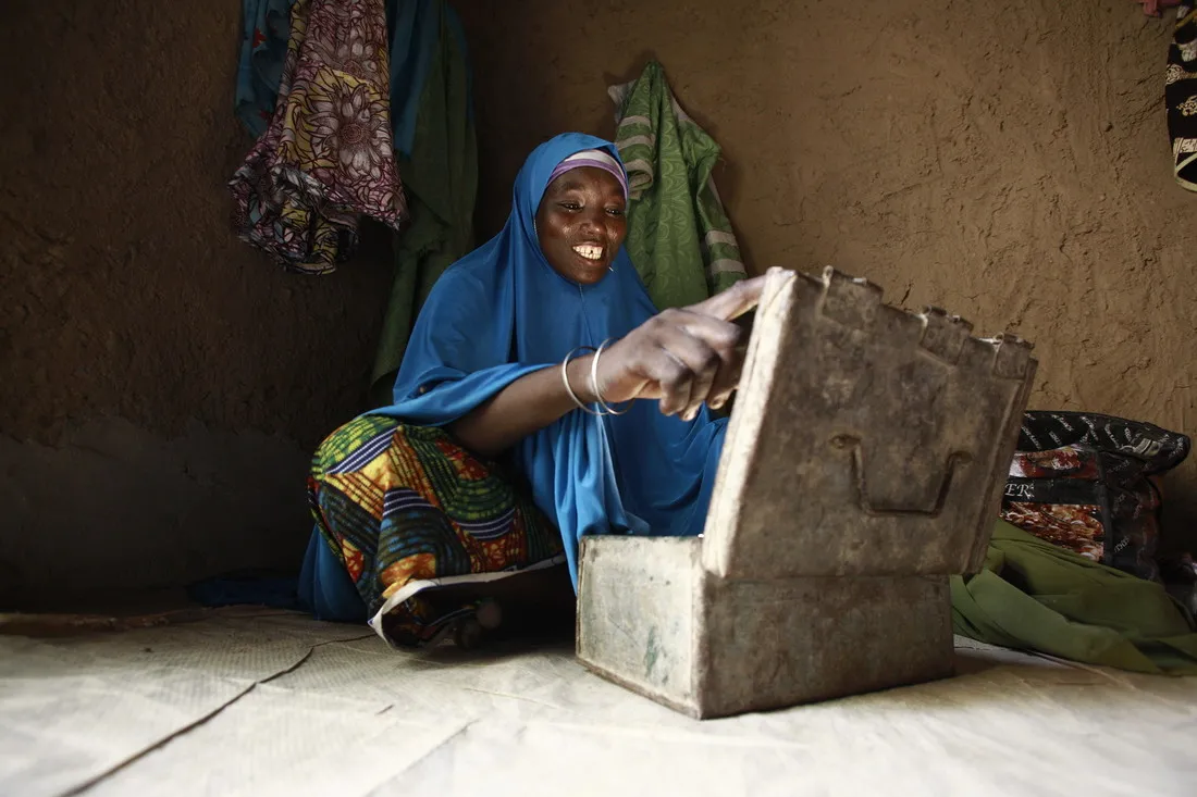 A woman wearing bright royal blue smiles as she opens a metal box on the floor.