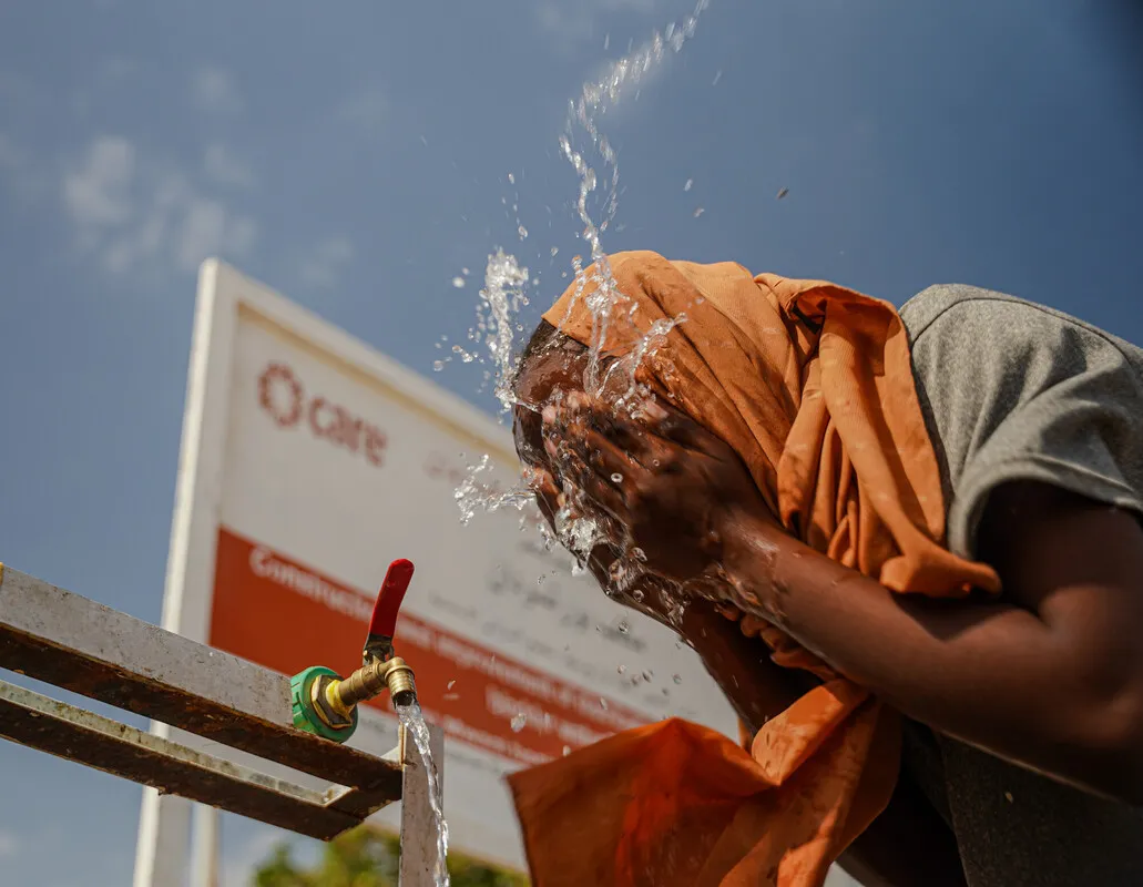 A girl washing her face with water with Care sign in background.