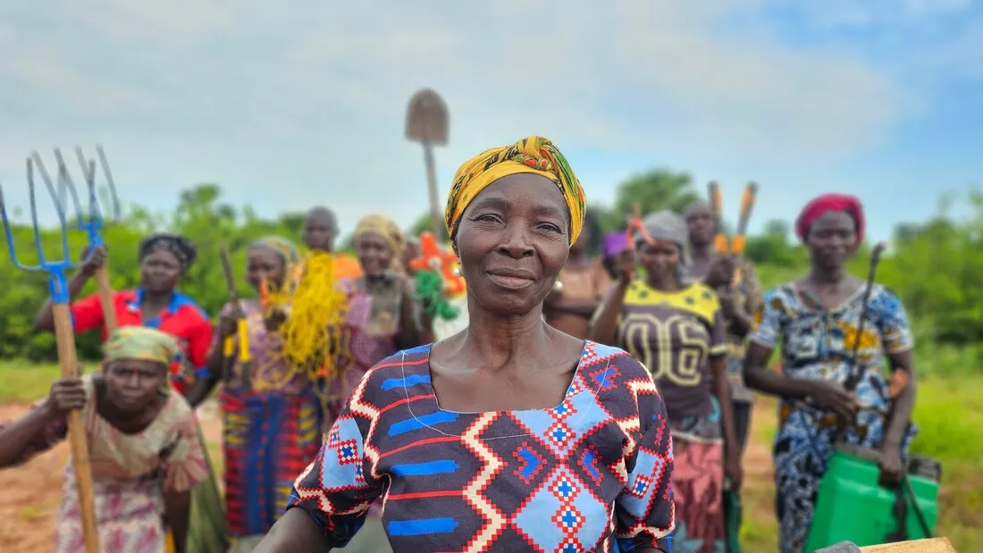 One woman leads a group of women carrying farming tools.