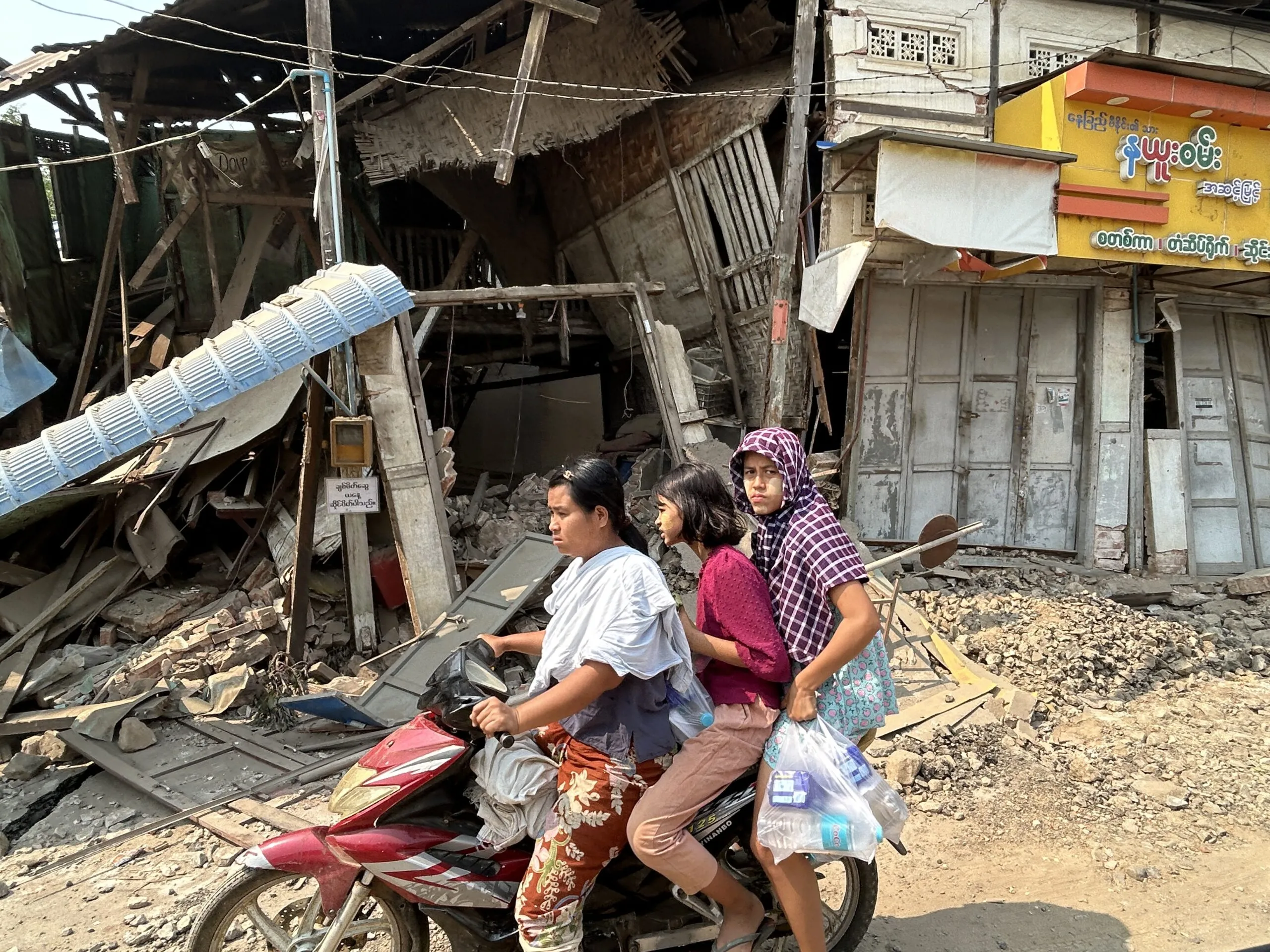 Three people on a motorbike pass destroyed buildings in Mandalay.