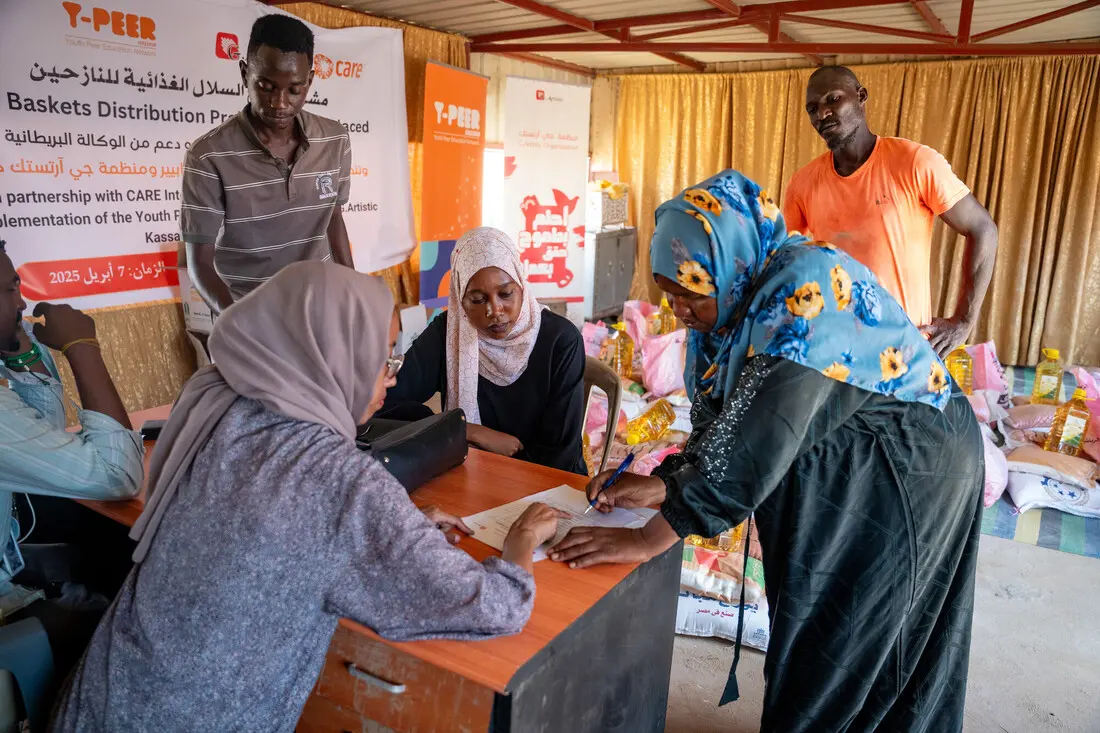 A woman completes a form at a desk, while two other women speak with her.