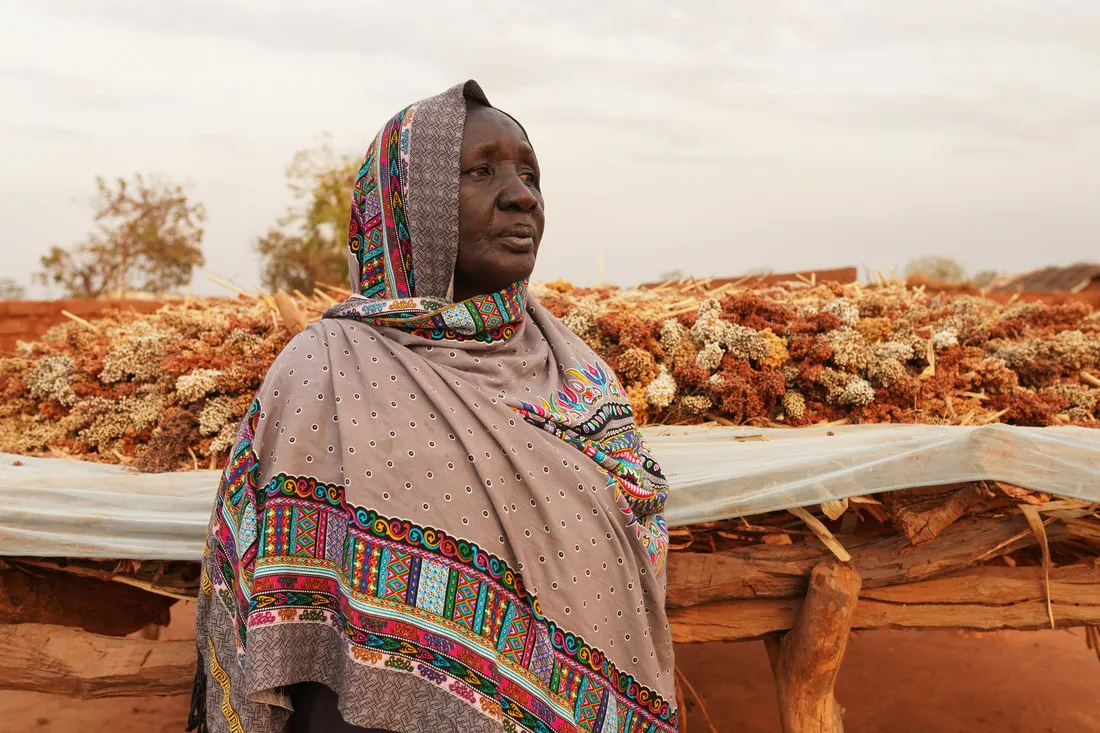 A woman affected by the South Sudan humanitarian crisis looks off into the horizon. Behind her, dried flowers have been laid out across a white tarp.