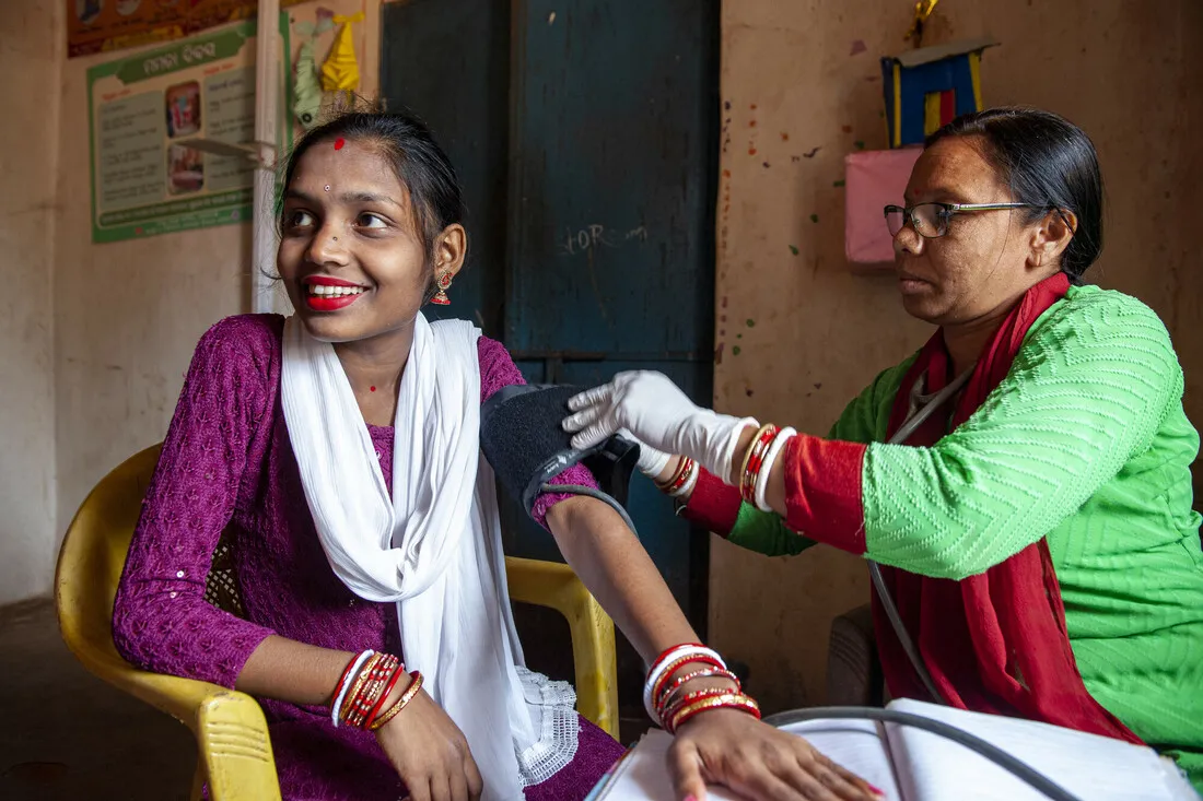 A woman having a blood pressure cuff around her arm being checked by a healthcare worker.