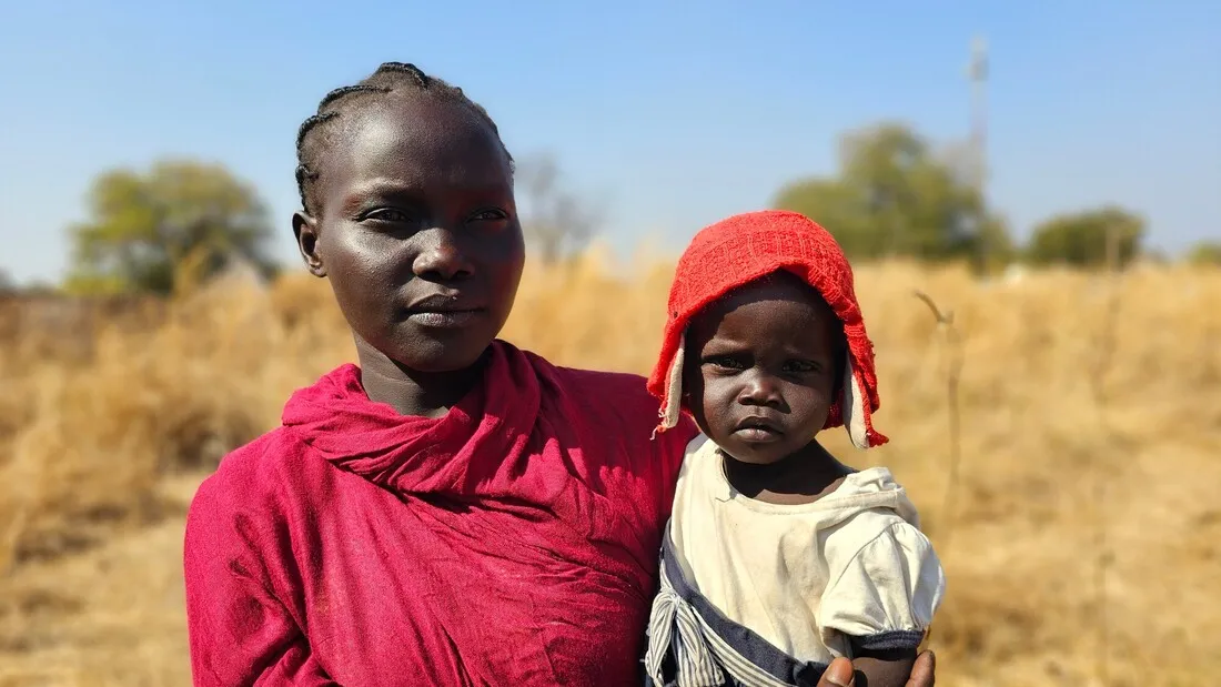 A mother holds her small child in front of a field.